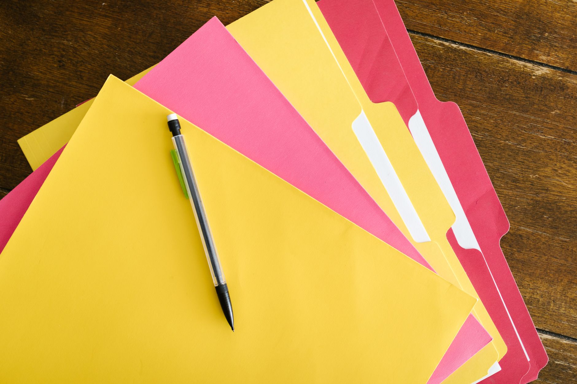 Colourful document folders and a pen on a wooden table.