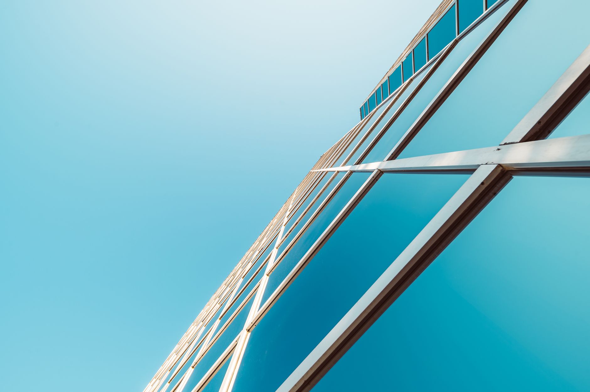 The glass facade of a contemporary building seen from below against a clear blue sky.