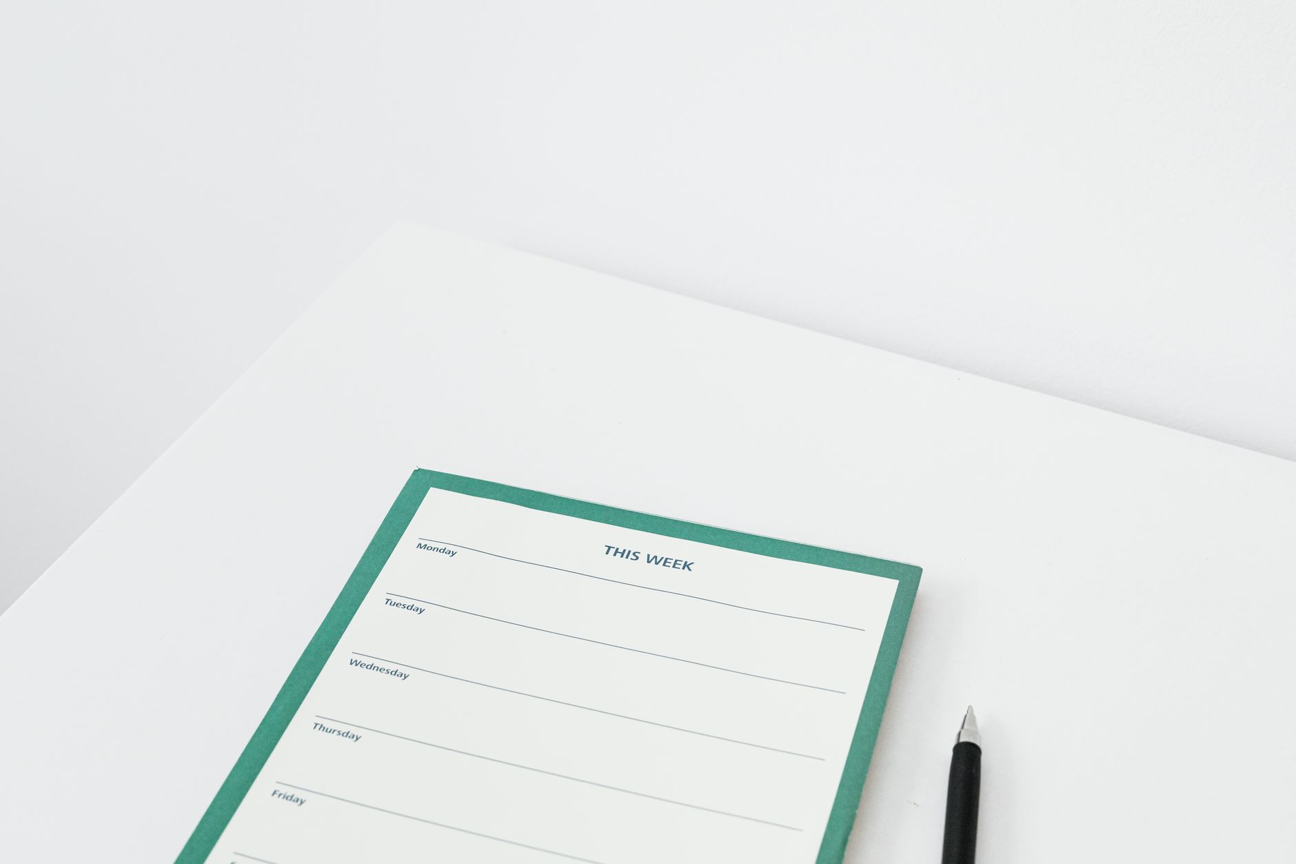 A weekly planner page and a pen on a white desk.