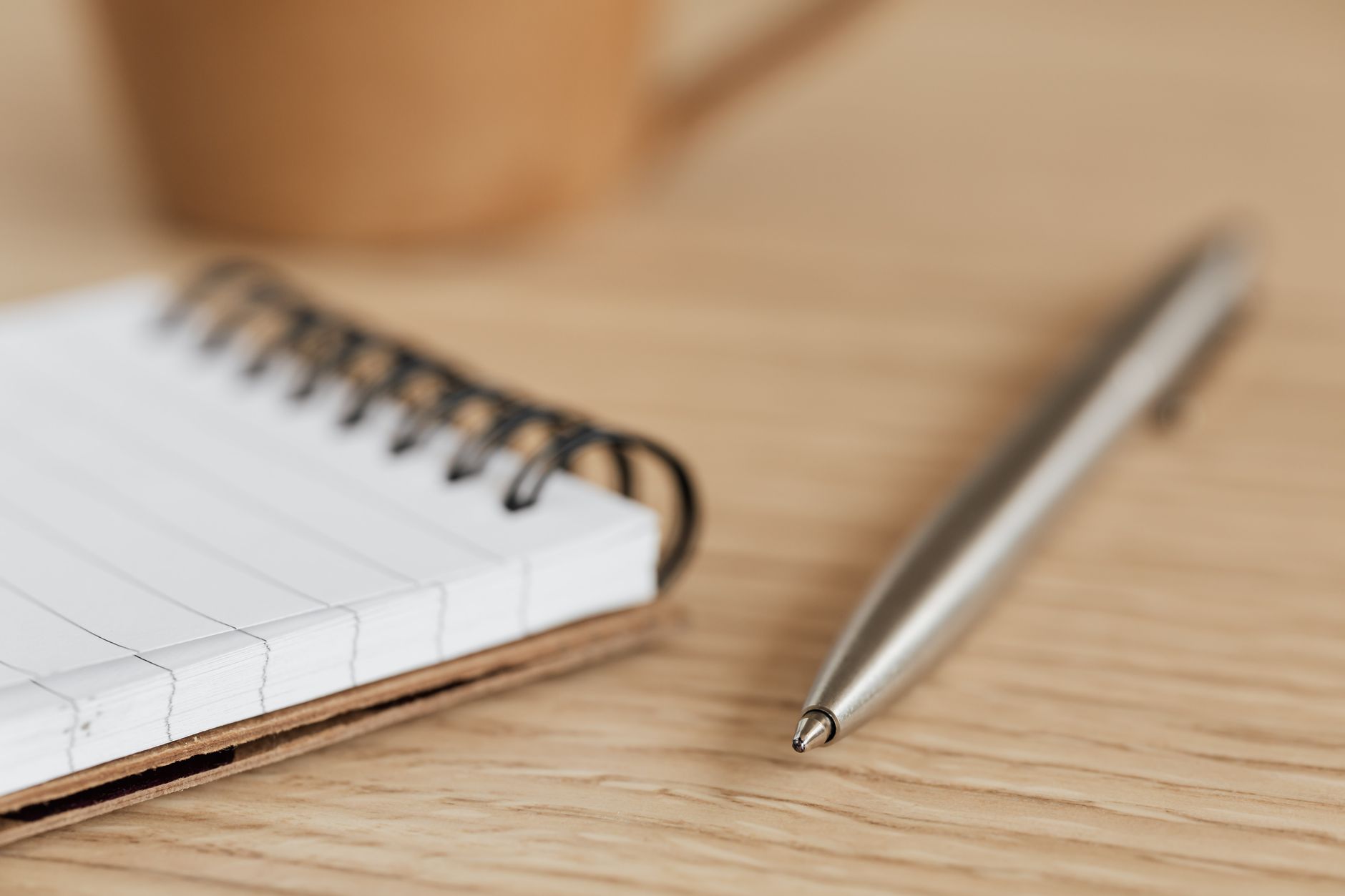 A spiral notepad and a metal pen on a wooden desk, close up.