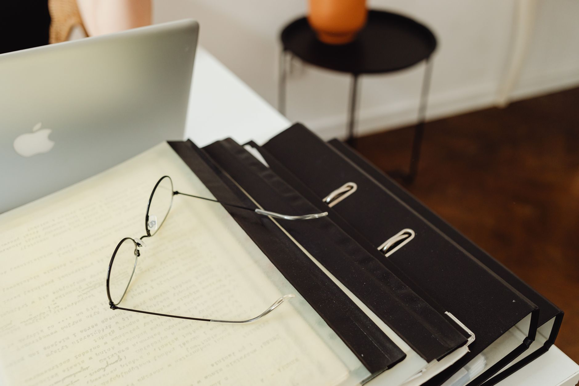 Binders and loose application documents beside a laptop on an office desk