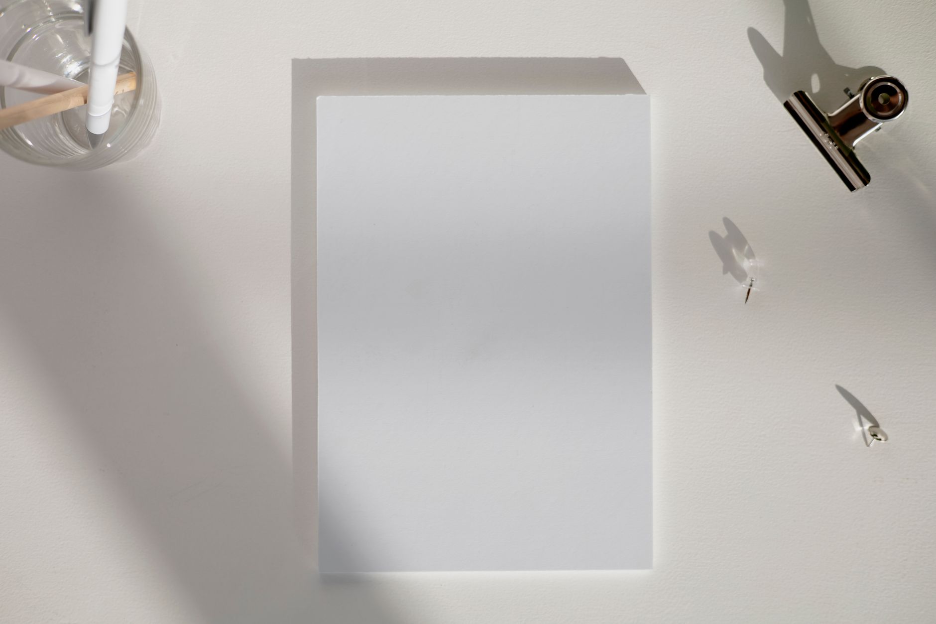 A blank sheet of paper, a pen and a binder clip on a white desk, seen from above.