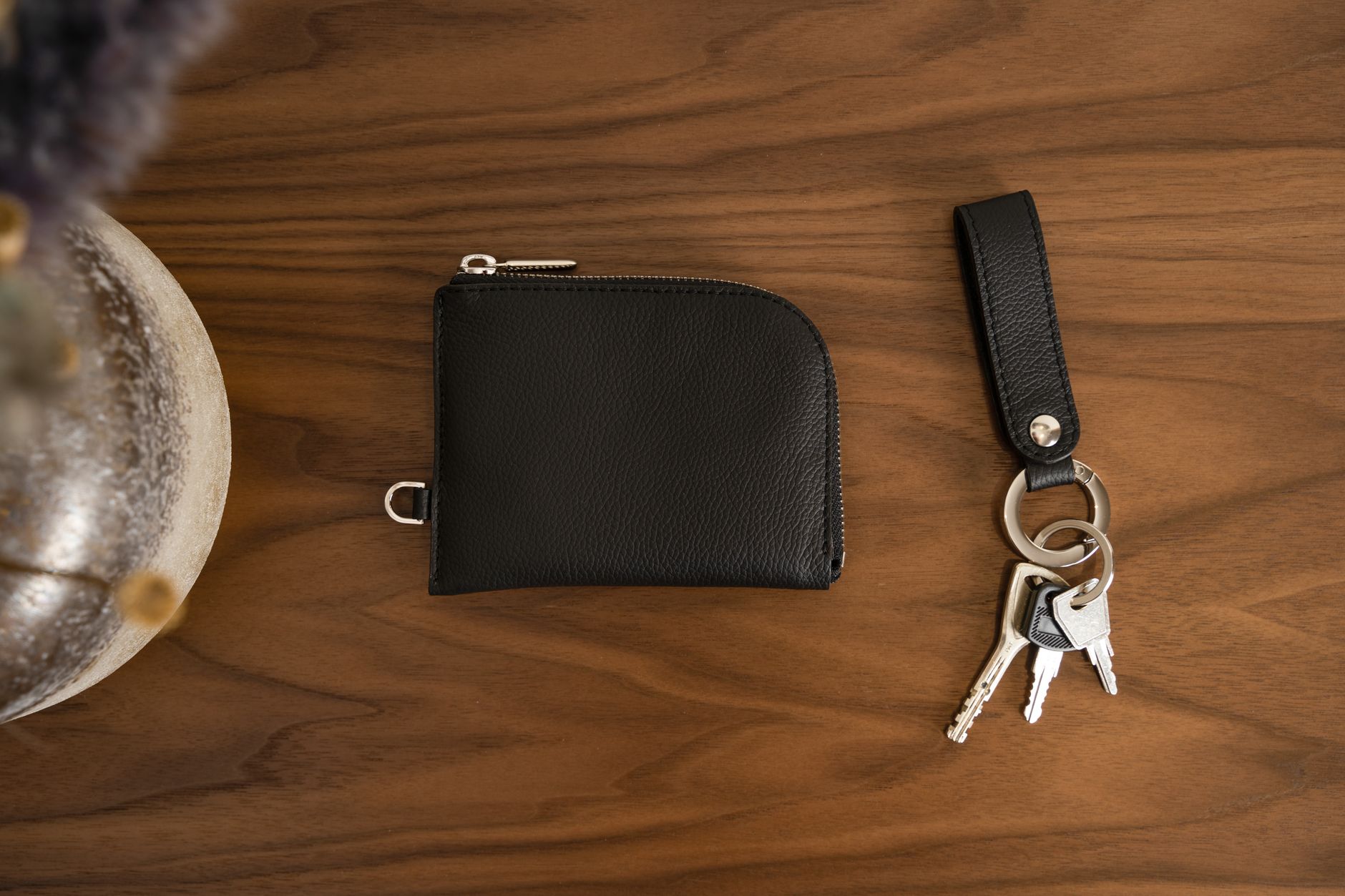 A black leather wallet and a set of keys on a wooden table.