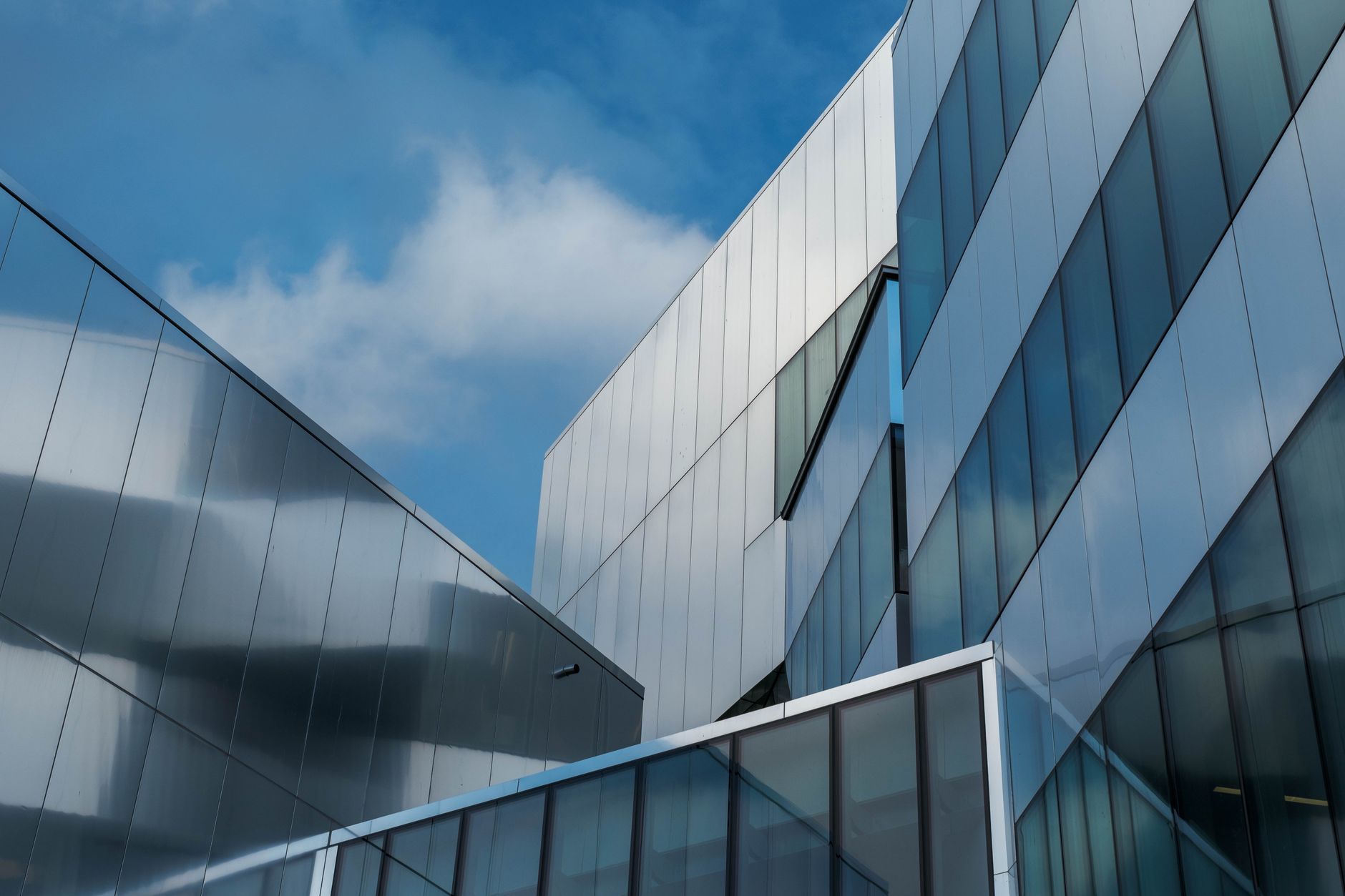 Modern glass and metal buildings seen from below under a blue sky with clouds
