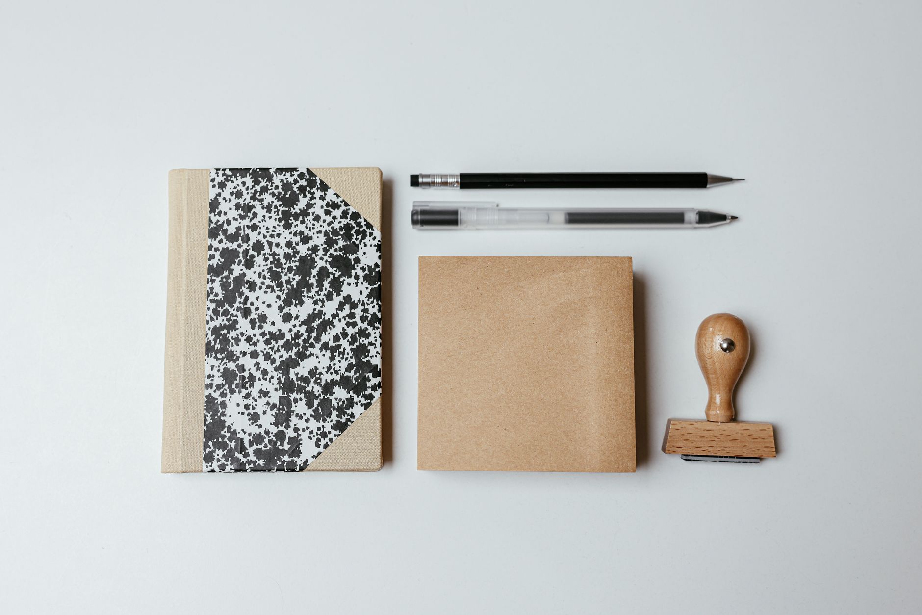 A flat lay of a notepad, pens and a wooden rubber stamp on a clean background.