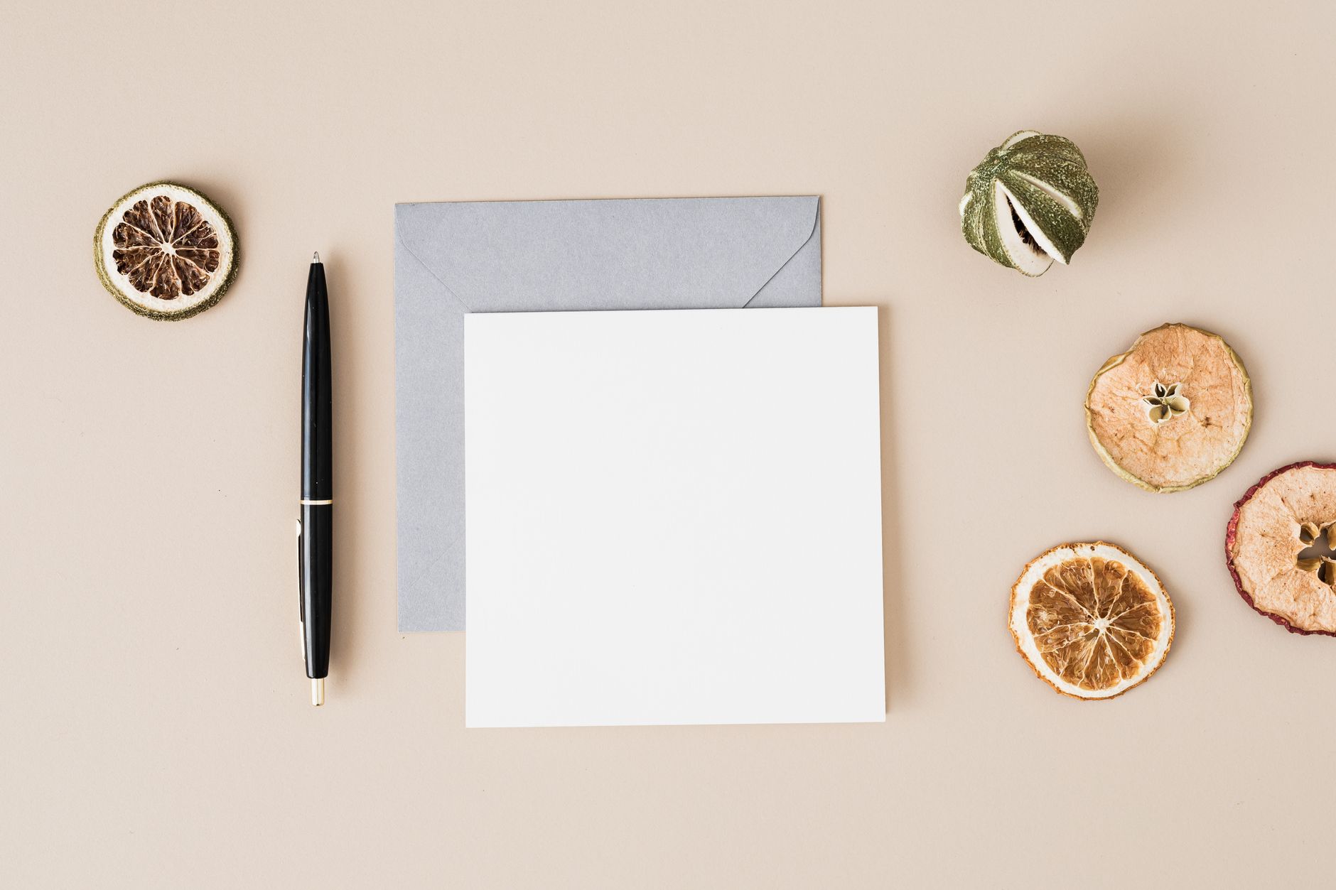 A blank card on a grey envelope beside a black pen and dried fruit slices.