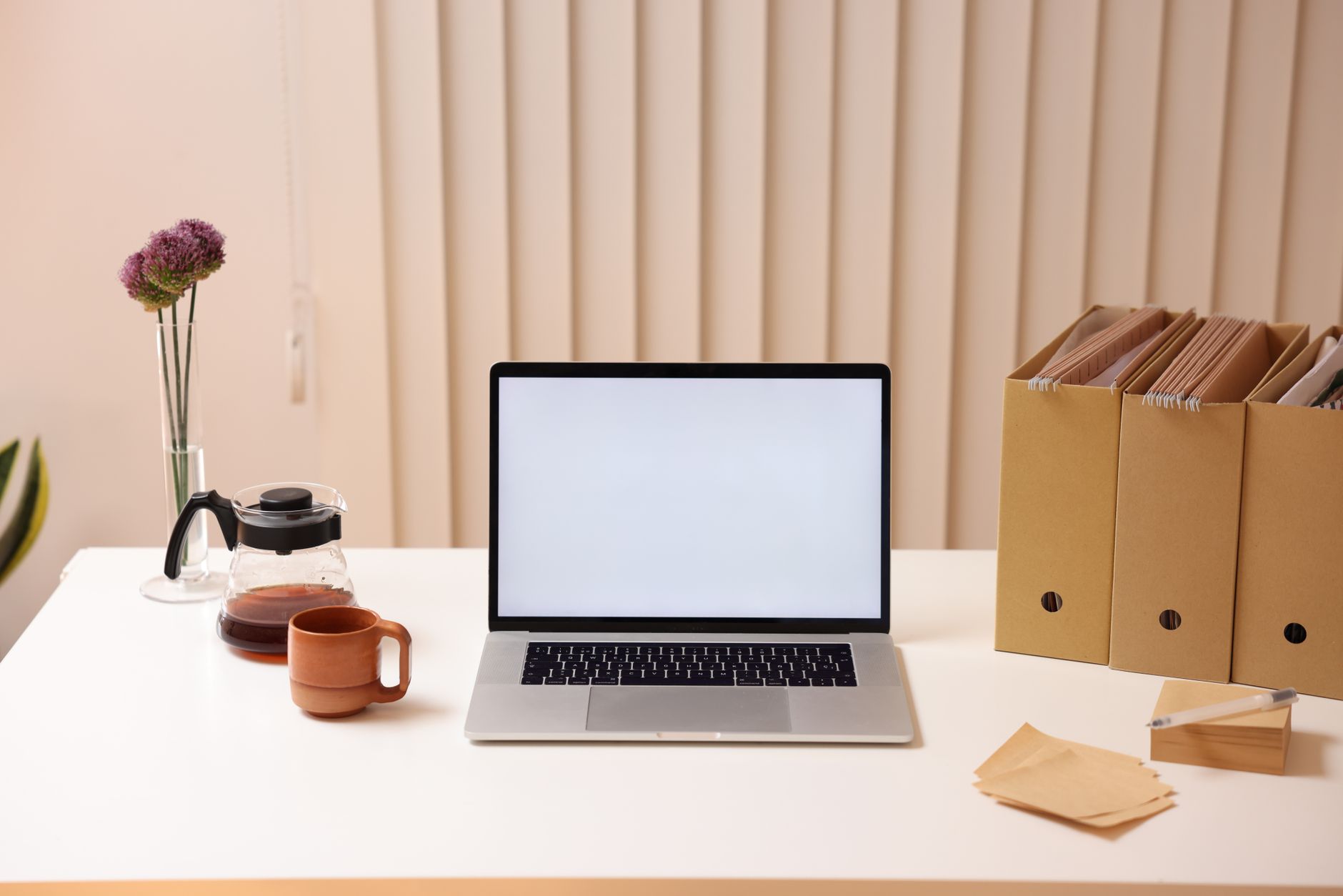 A laptop with a blank screen beside beige folder organizers on a white desk.