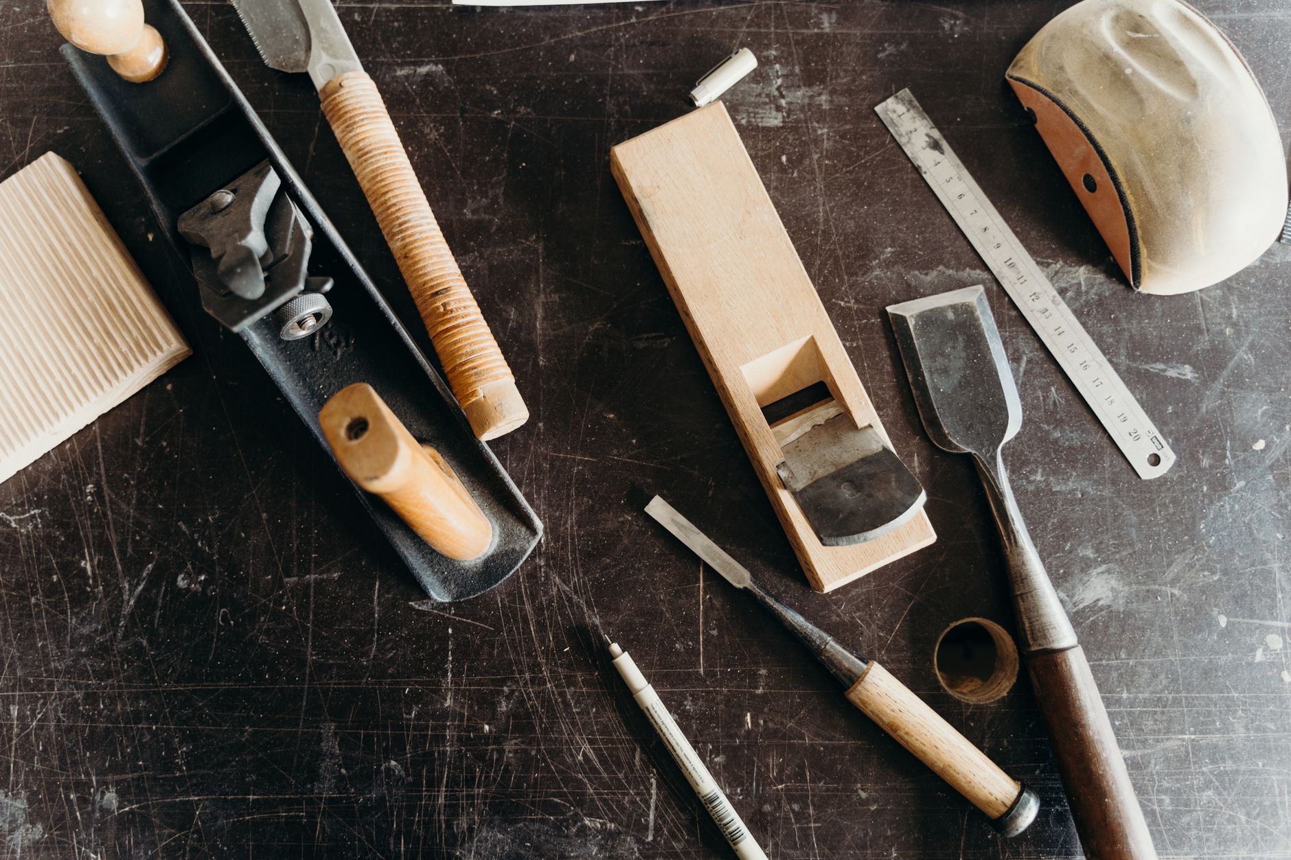 Woodworking tools on a dark workshop table, seen from above.