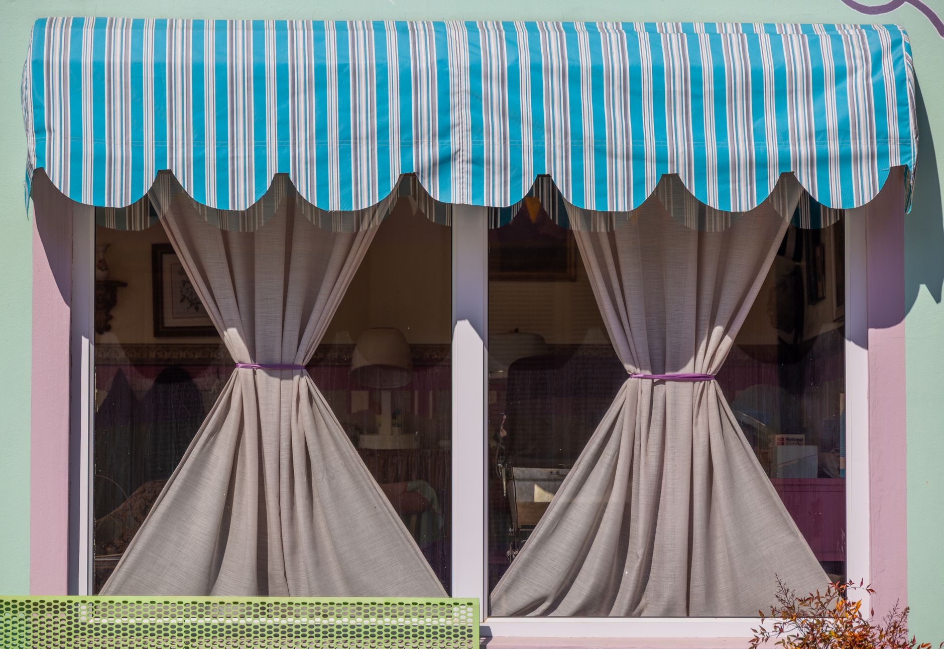 A window with a blue striped awning and tied-back curtains.