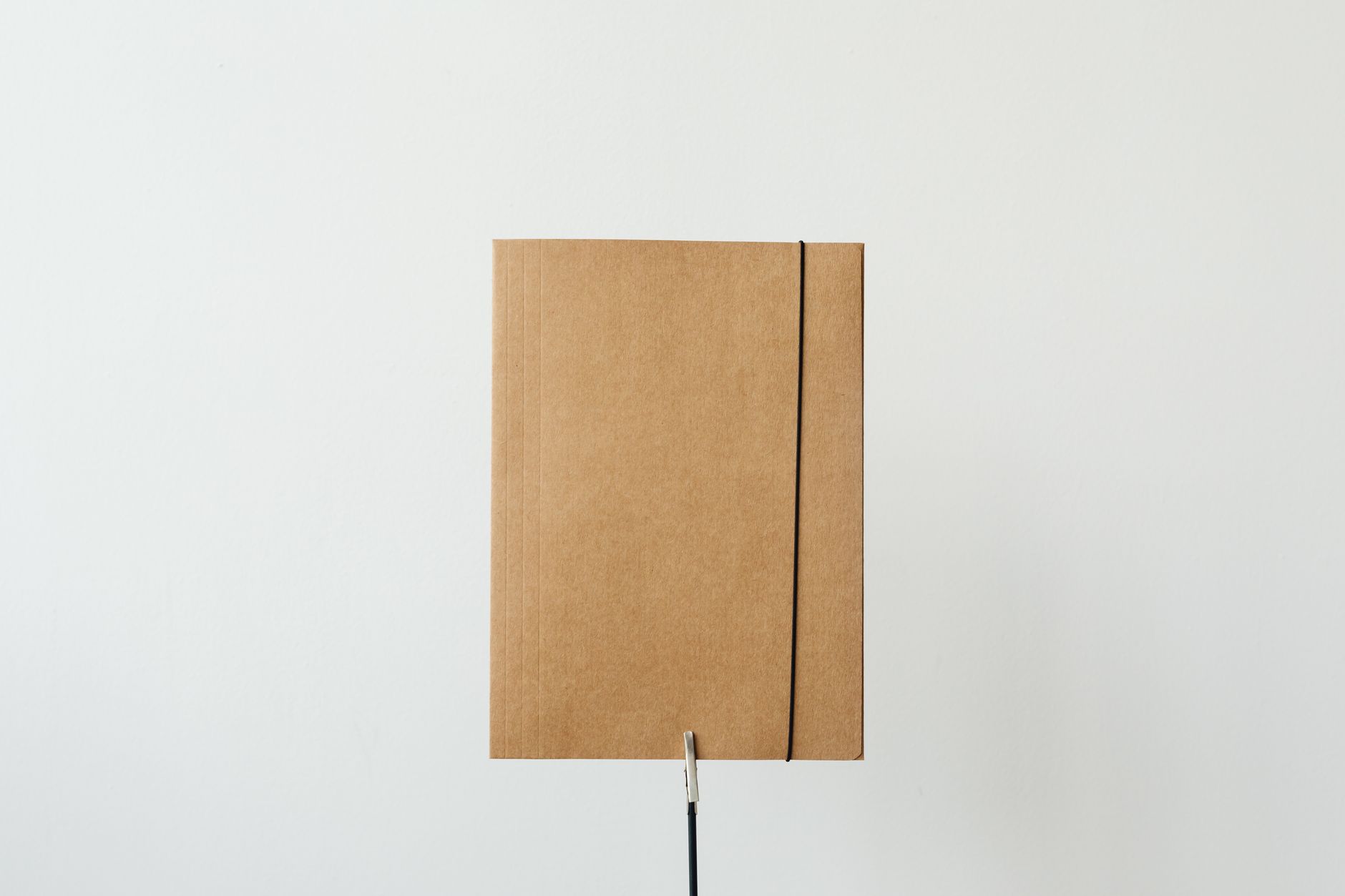 A plain cardboard folder closed with an elastic band against a white wall.