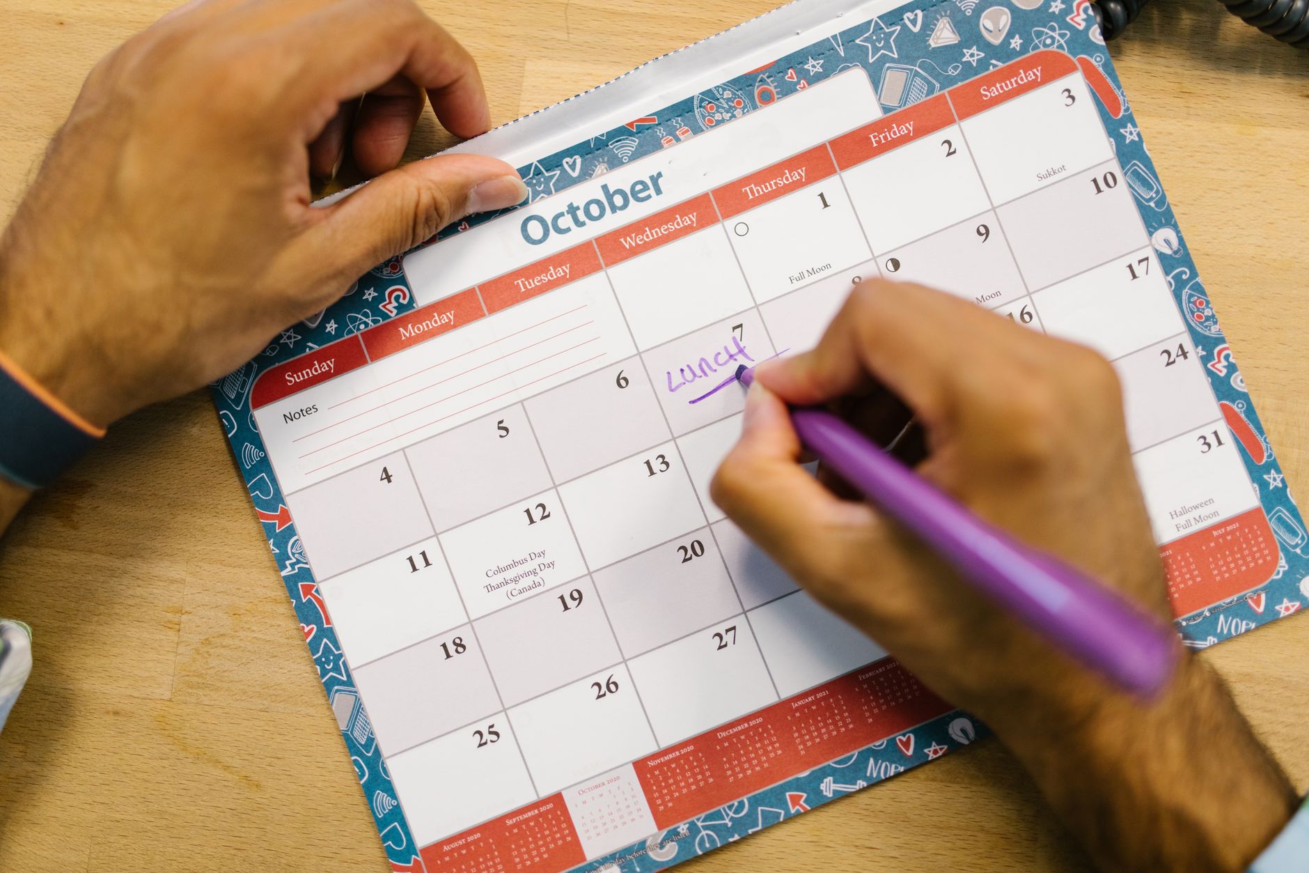 A paper calendar with a notebook and a pen on a desk.